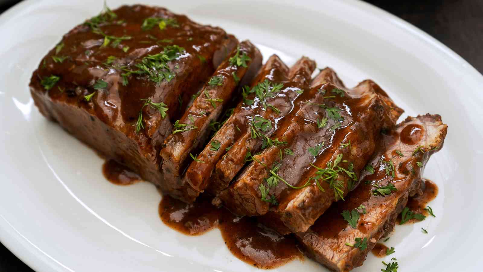 Sliced roast beef with brown gravy and chopped herbs served on a white oval plate.