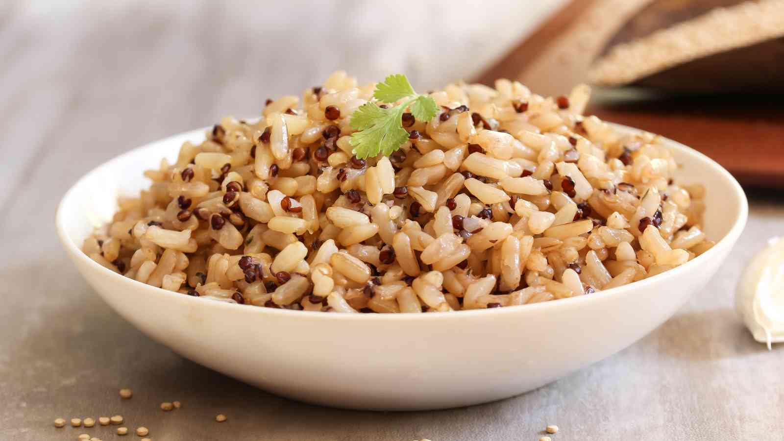 A white bowl filled with cooked brown rice mixed with black quinoa, garnished with a sprig of cilantro.