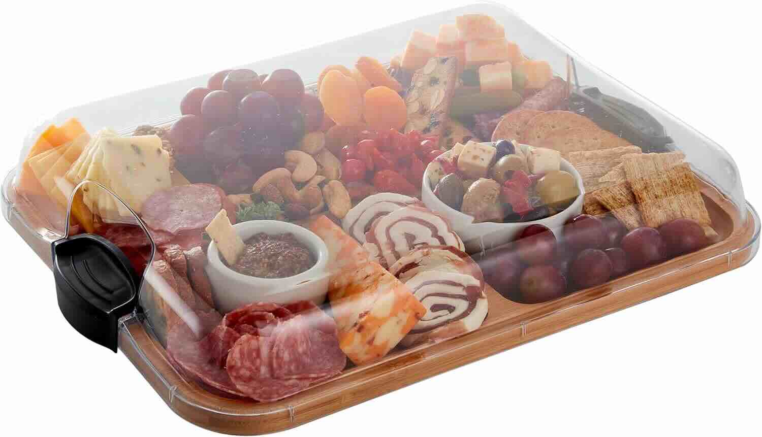 A covered wooden tray with assorted cheeses, meats, crackers, grapes, nuts, dried fruits, olives, and dips arranged neatly inside.