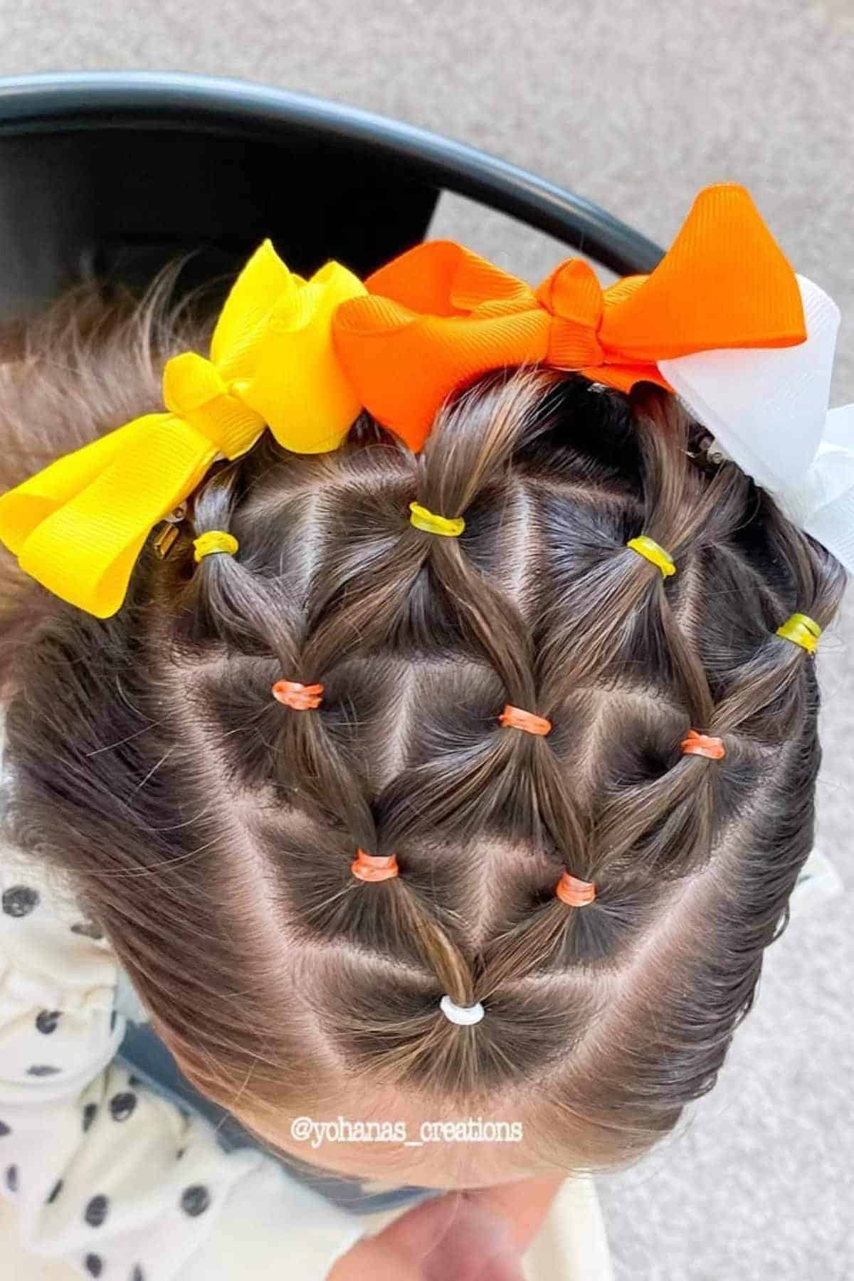 Top view of a child's hair styled in a cute pattern with small colorful elastics and large yellow, orange, and white bows.