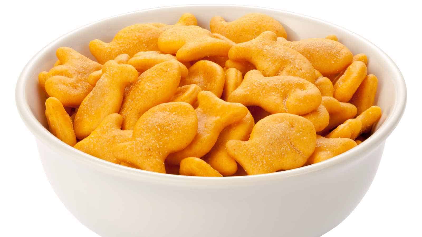 A white bowl filled with orange, fish-shaped cheese crackers against a plain white background.