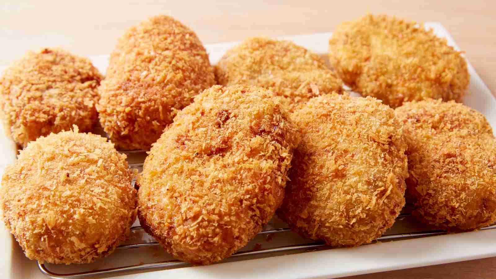 A plate with several golden-brown, breaded and fried croquettes arranged closely together.