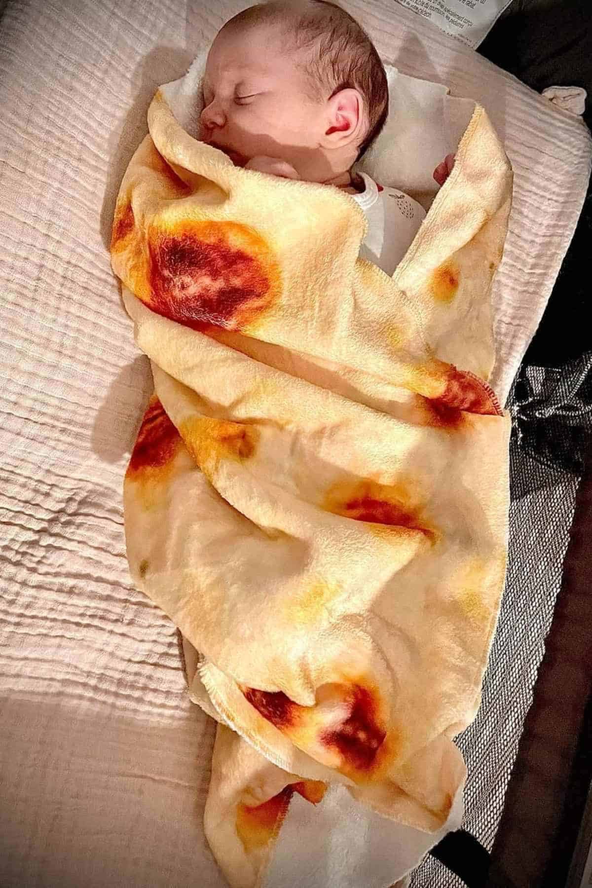 A baby is sleeping, wrapped in a blanket that resembles a scrambled egg.