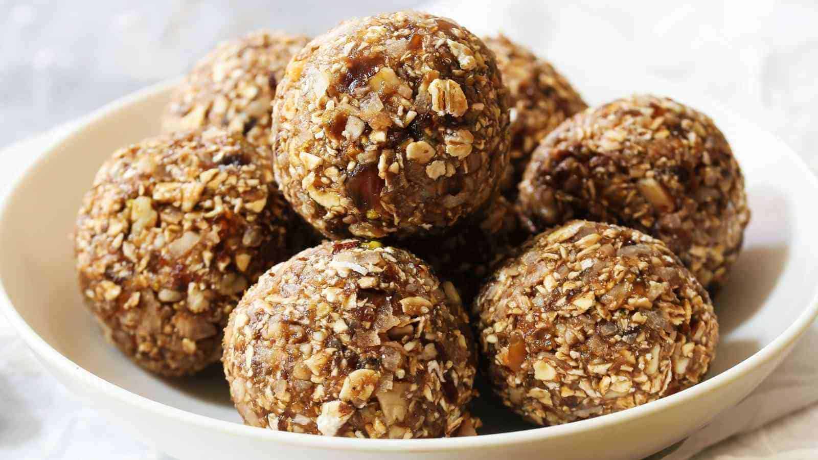 A white bowl filled with several round, oat and nut energy bites made from oats, nuts, and dried fruit.
