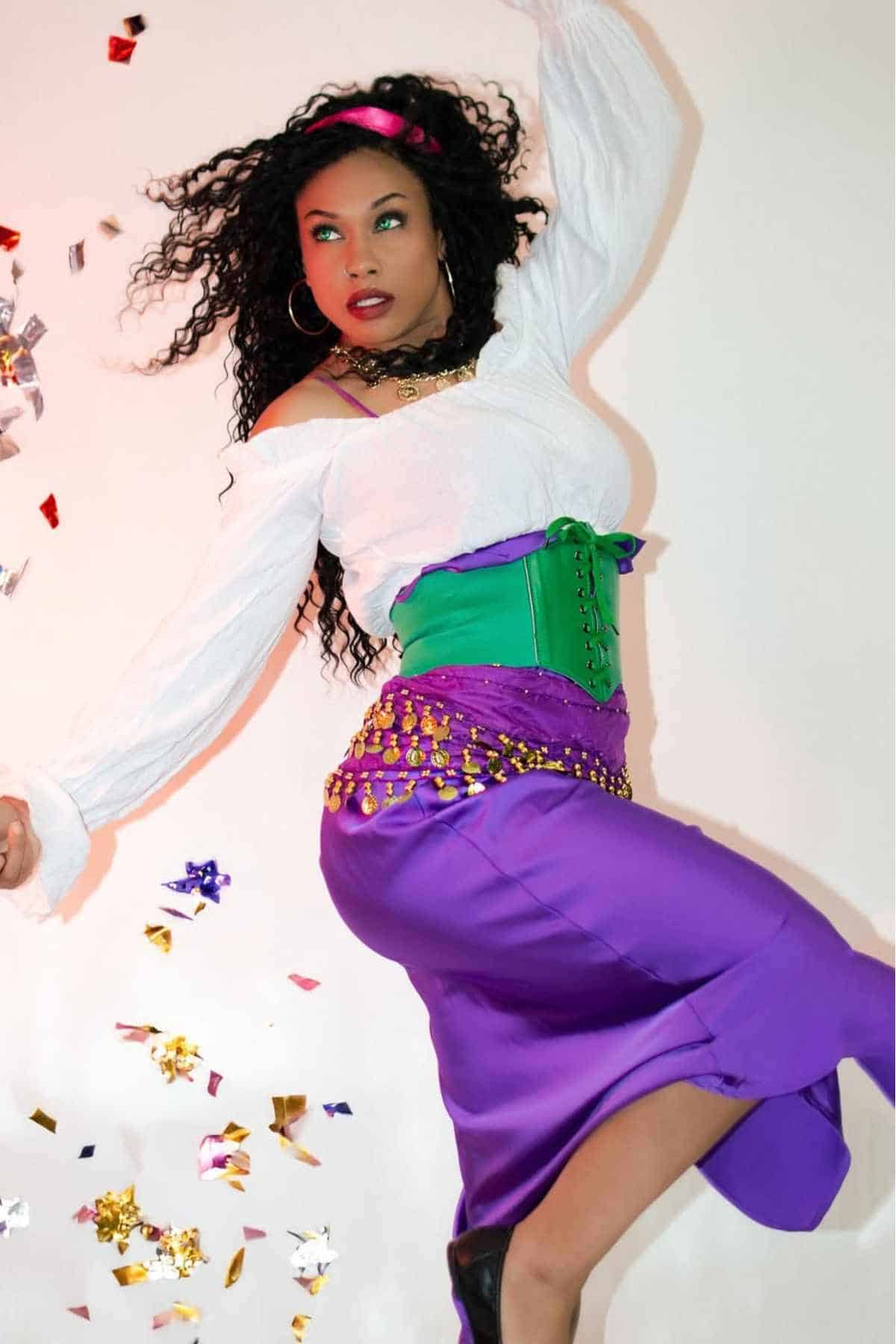 A woman in a white blouse, green corset, and purple skirt poses against a white background with colorful confetti falling around her.