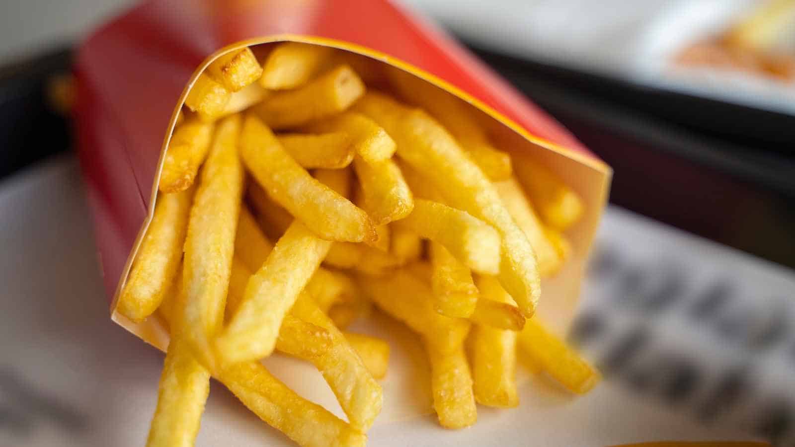 A serving of golden French fries in a red paper container, placed on a white surface.