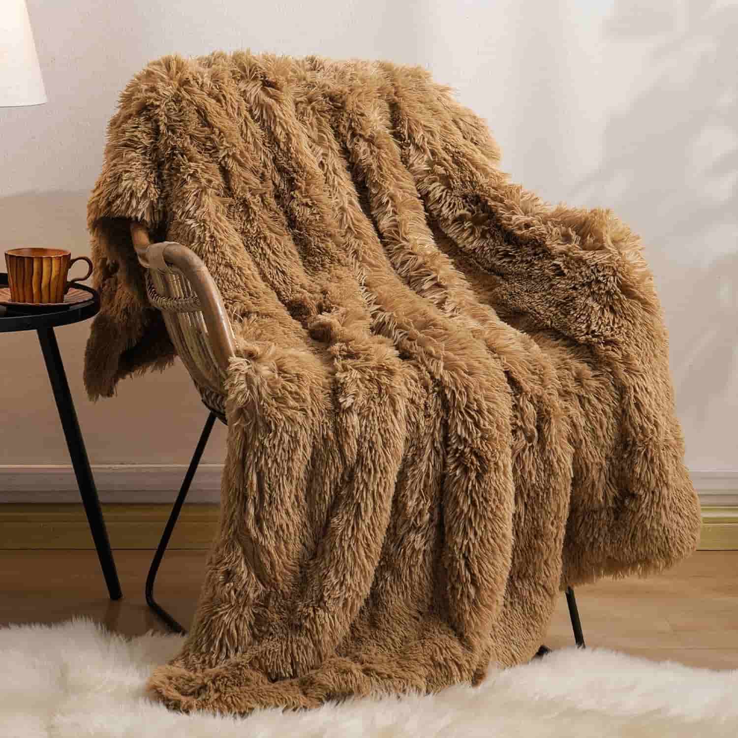 A large, fluffy brown faux fur blanket draped over a chair next to a small round side table with a mug on it, on a light-colored floor with a white rug.