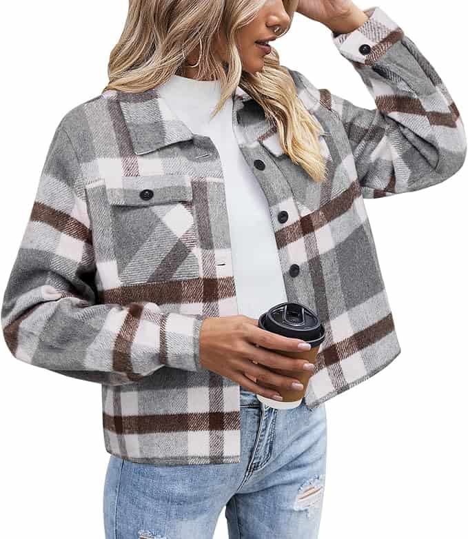 A woman wearing a gray, white, and brown plaid jacket over a white top, holding a takeaway coffee cup, and dressed in ripped light blue jeans.