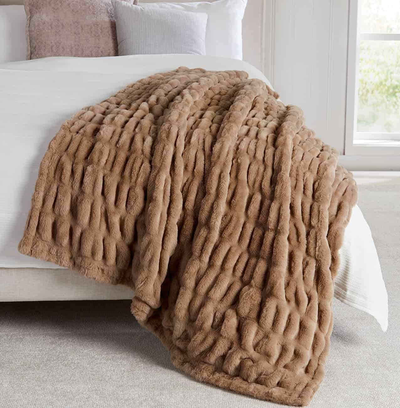 A textured brown faux fur throw blanket draped over the side of a neatly made bed in a bright, modern bedroom.