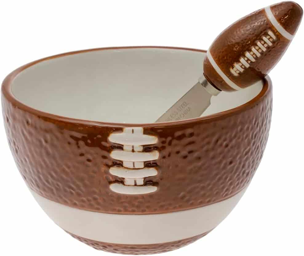 A ceramic bowl designed to resemble a football, with a matching spreader featuring a football-shaped handle placed inside.