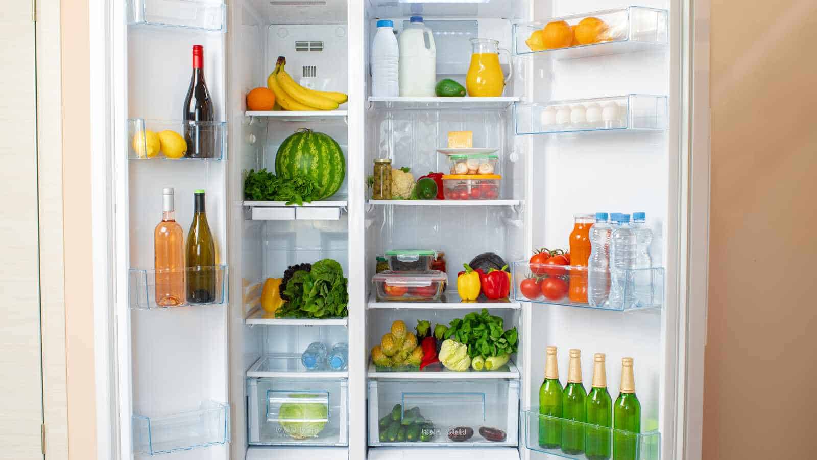An open refrigerator filled with fruits, vegetables, bottled drinks, eggs, dairy products, and various containers of food.