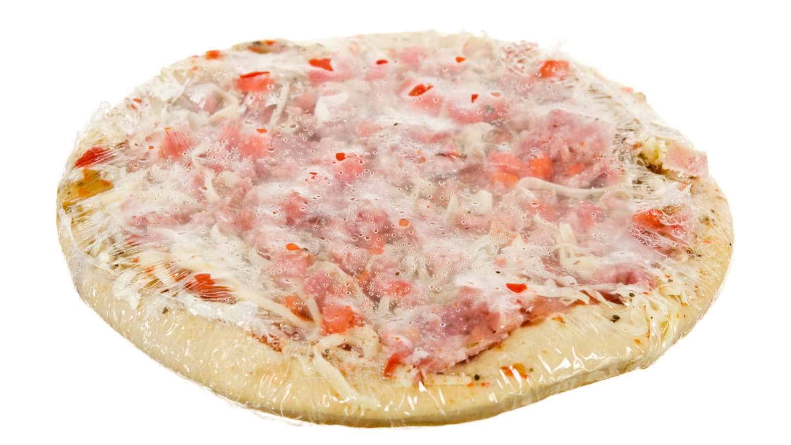 Frozen, uncooked pizza with visible toppings, wrapped tightly in clear plastic on a white background.
