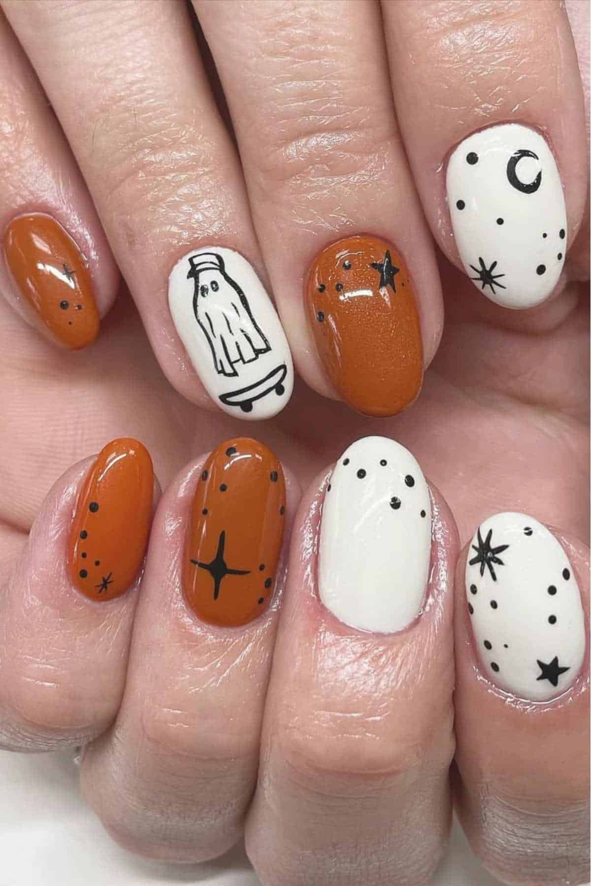 Fingernails painted in white and orange with black Halloween-themed designs, including a ghost, stars, dots, and a crescent moon.