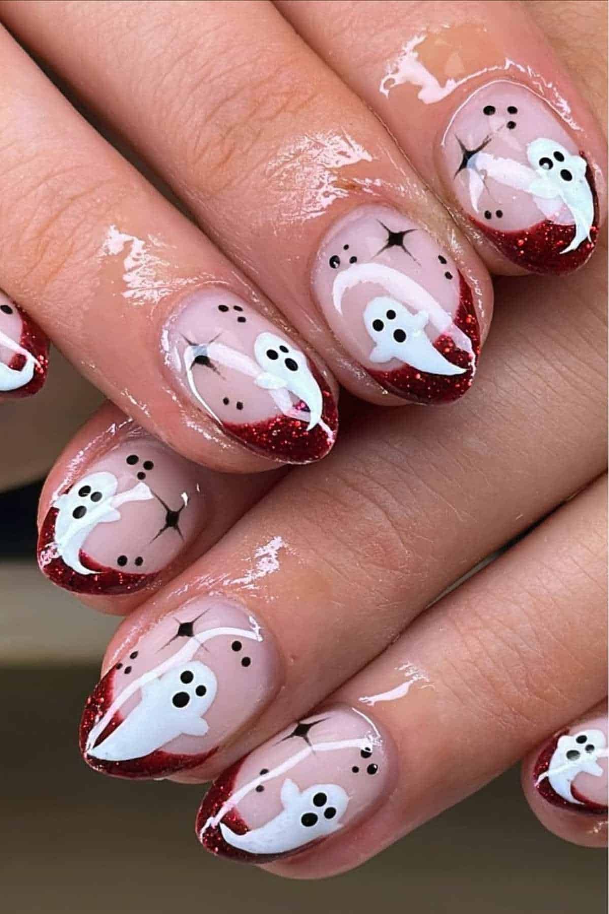 Fingernails with Halloween-themed nail art featuring white ghosts and red glittery French tips.