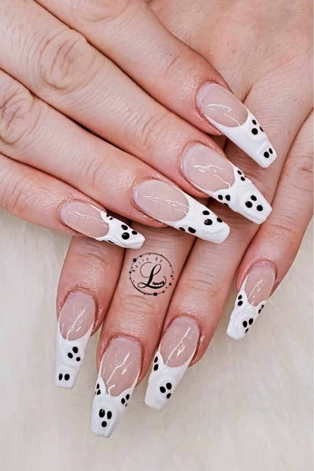 Hands with long, clear acrylic nails featuring white tips and small black dots, arranged to resemble ghost faces, displayed on a white background.