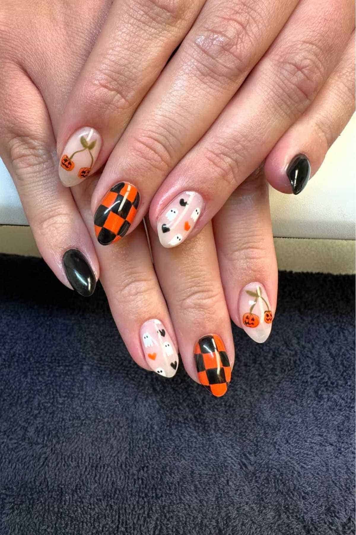 Hands with Halloween-themed nail art featuring black, orange, and white designs, including pumpkins, ghosts, checkerboards, and plain black polish.