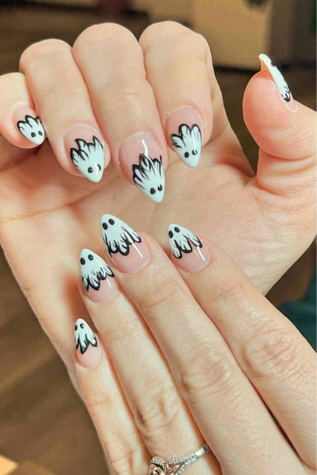 Close-up of hands with long nails featuring white and black ghost designs on each fingernail.