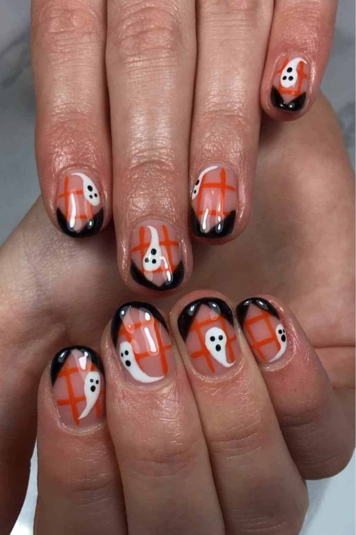 Fingernails with Halloween-themed nail art featuring small white ghost designs, orange grid backgrounds, and black-tipped French tips.
