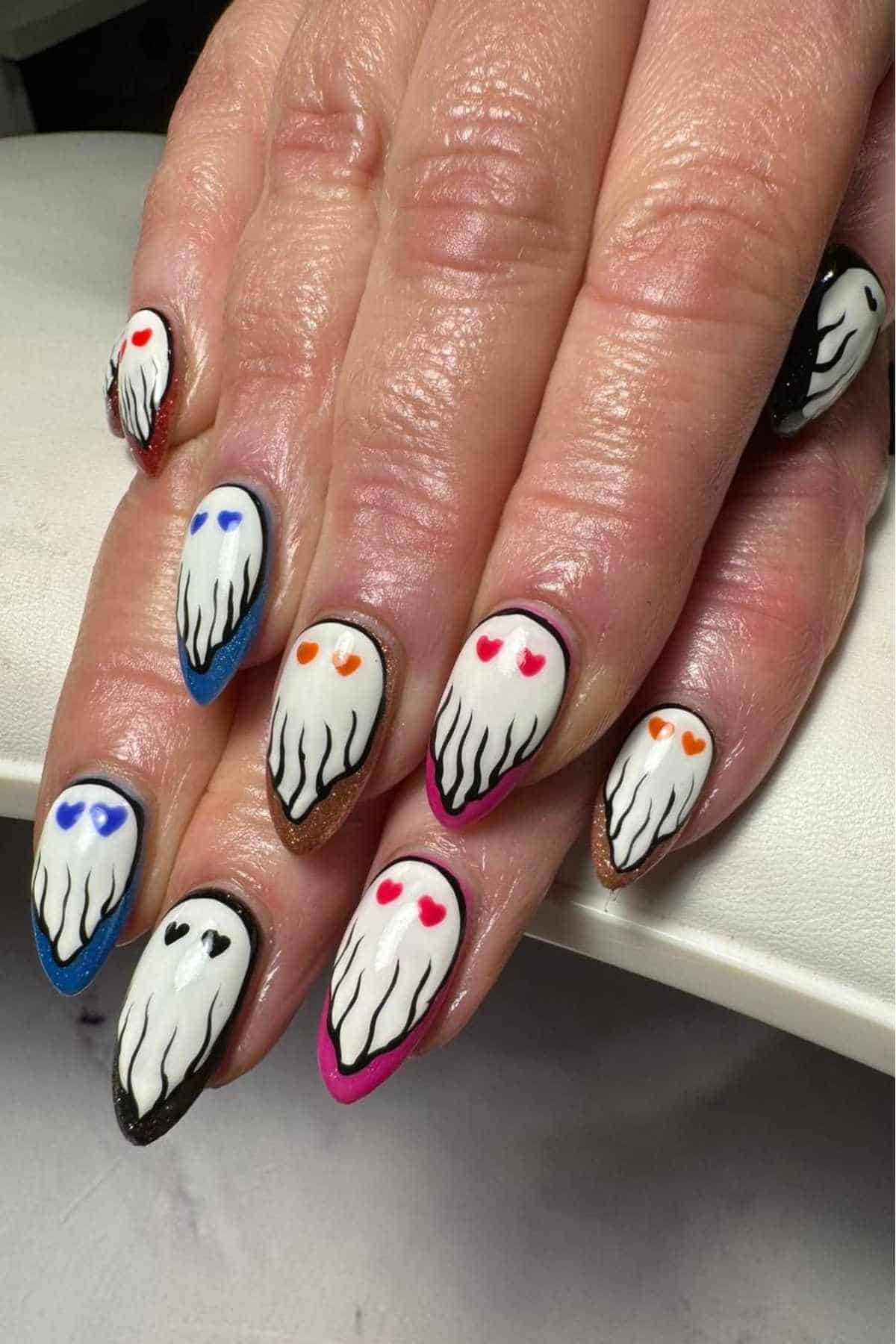 A hand with long nails painted with ghost designs; each ghost has heart-shaped eyes in different colors and outlines in various shades.