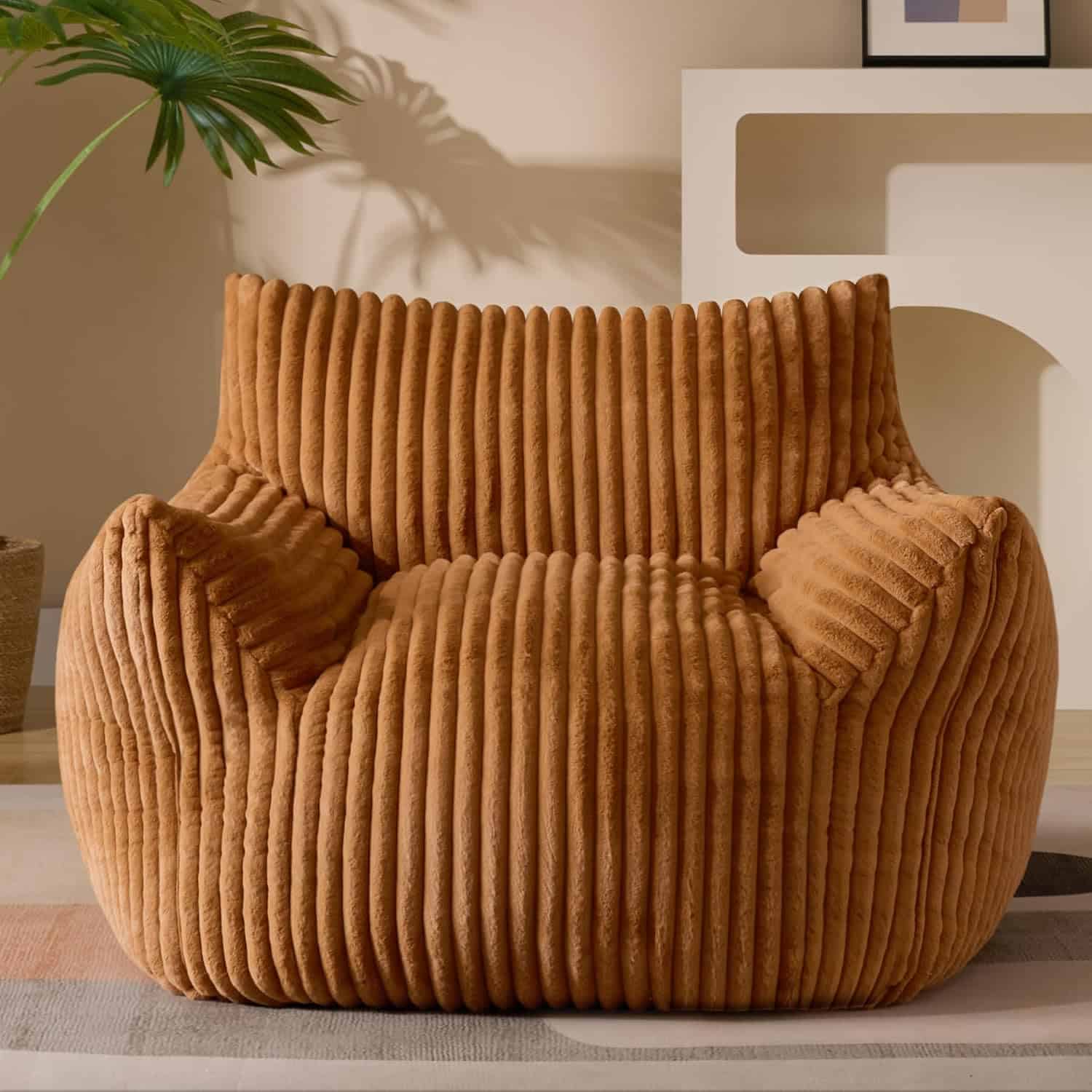 A large, brown, corduroy lounge chair with a ribbed texture sits in a modern room with neutral decor and a potted plant nearby.