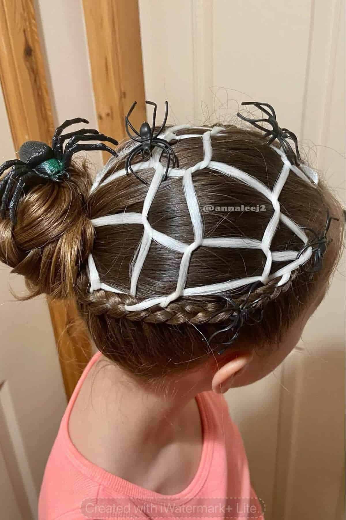 A girl's hair styled in a bun and braid with white ribbon arranged like a spider web, decorated with plastic black spiders.