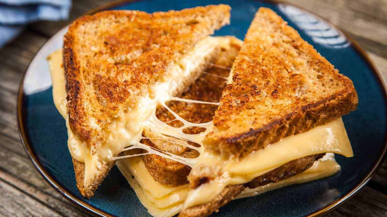 Two halves of a grilled cheese sandwich with melted cheese stretching between the slices, served on a blue plate.