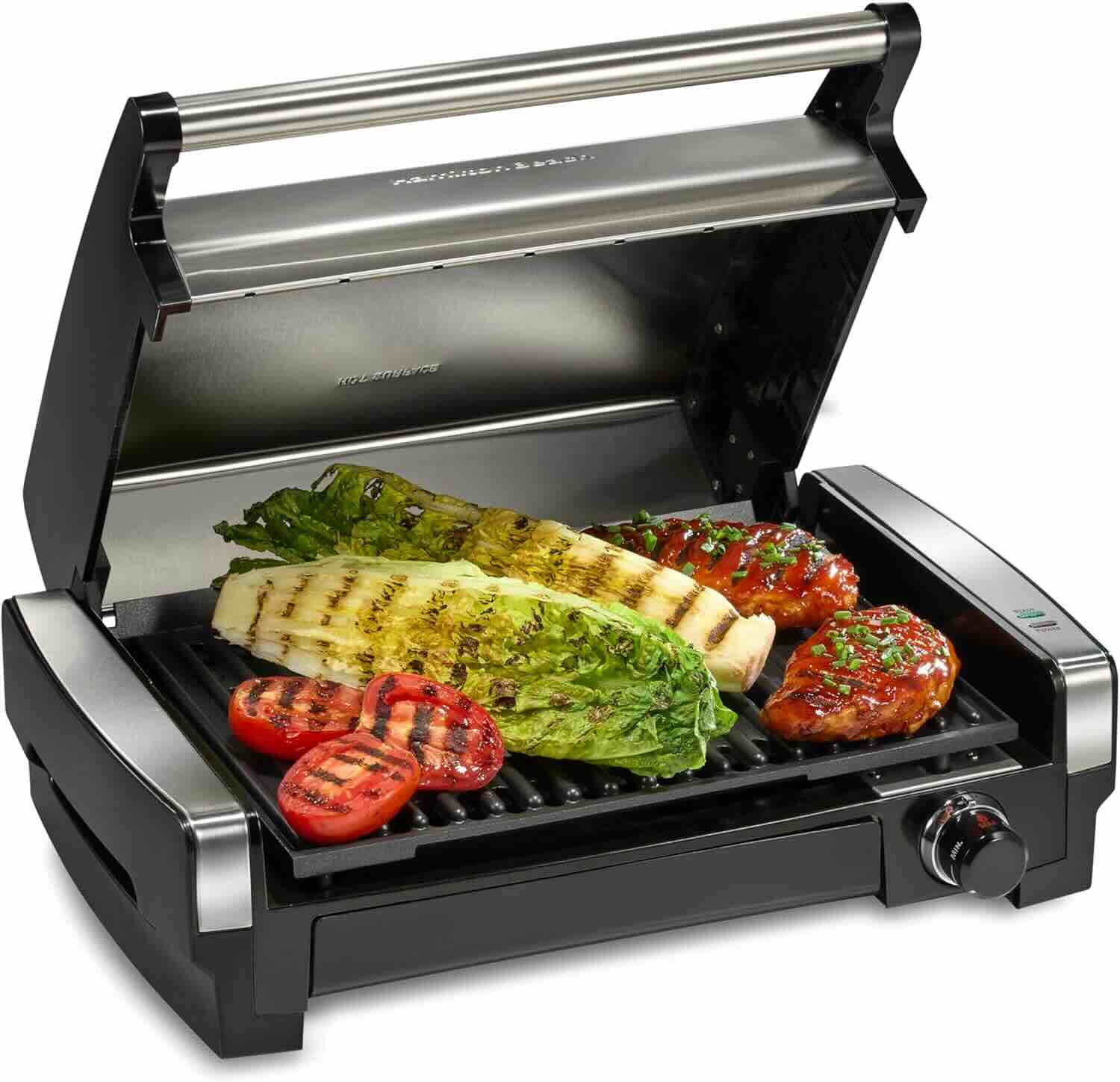 An electric indoor grill with the lid open, grilling romaine lettuce, tomato slices, and seasoned chicken breasts.