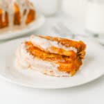 Three slices of pumpkin bread with icing are served on a white plate, with a fork and glass of milk in the background.