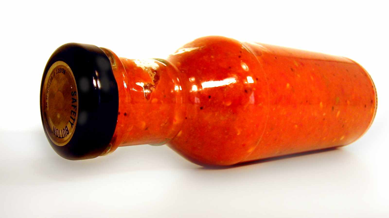 A glass bottle filled with bright red hot sauce lies on its side against a white background.