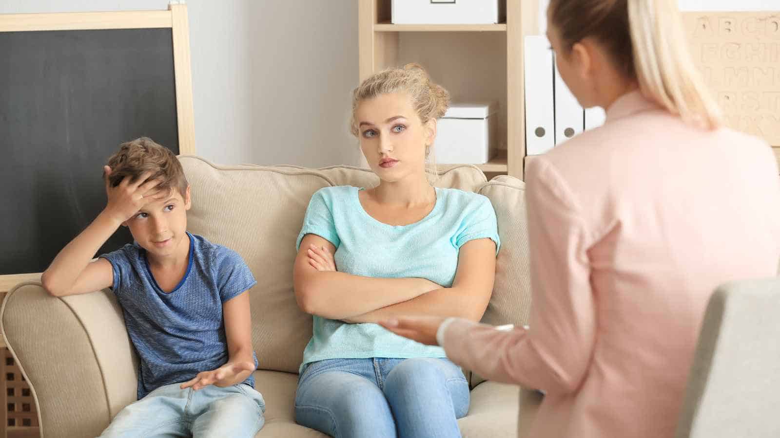 A woman and a boy sit on a couch facing another woman, possibly during a counseling or therapy session. The boy gestures with his hands while the woman has her arms crossed.