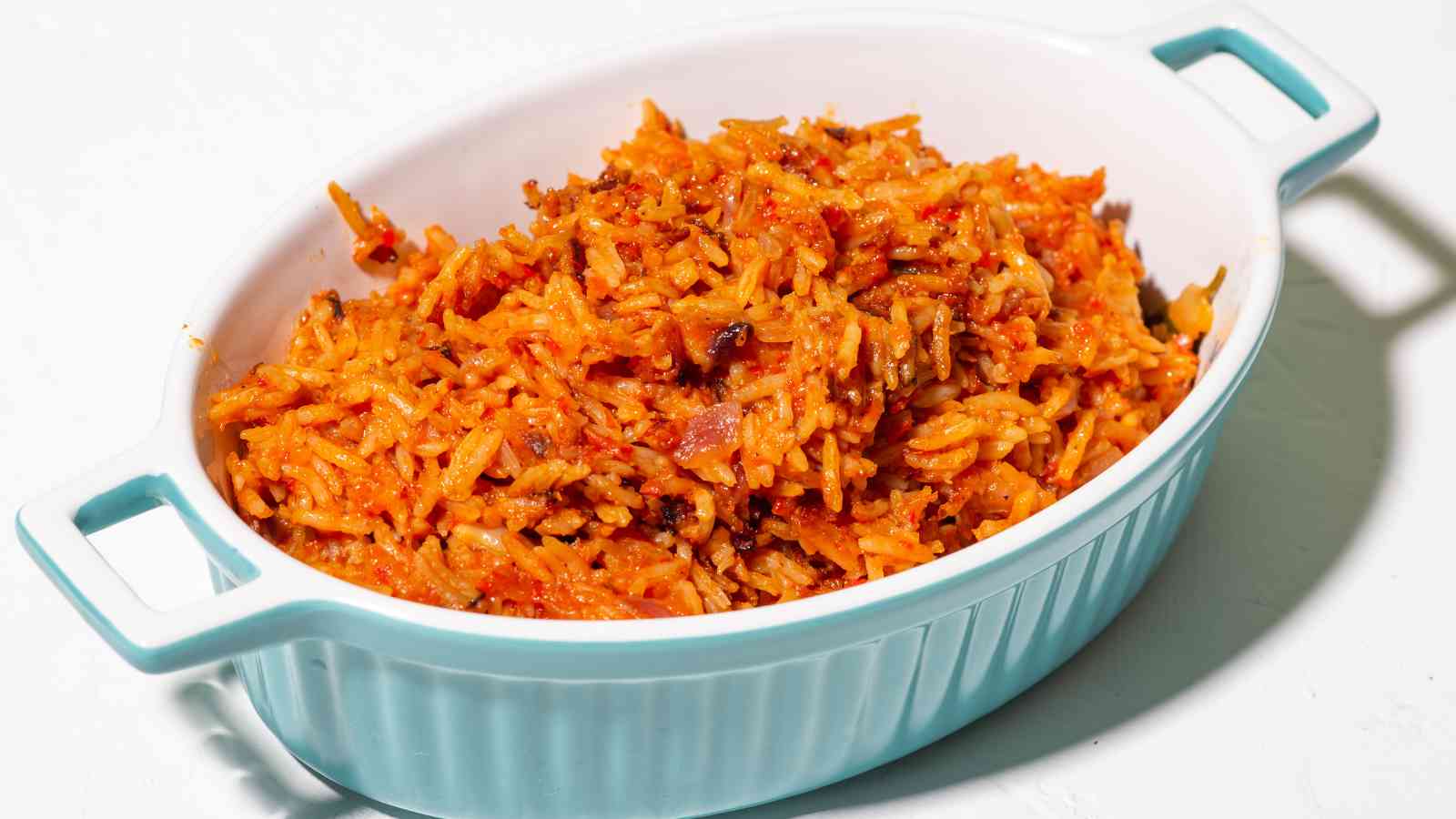 A white and blue dish filled with cooked orange-red rice mixed with visible pieces of onion and spices.