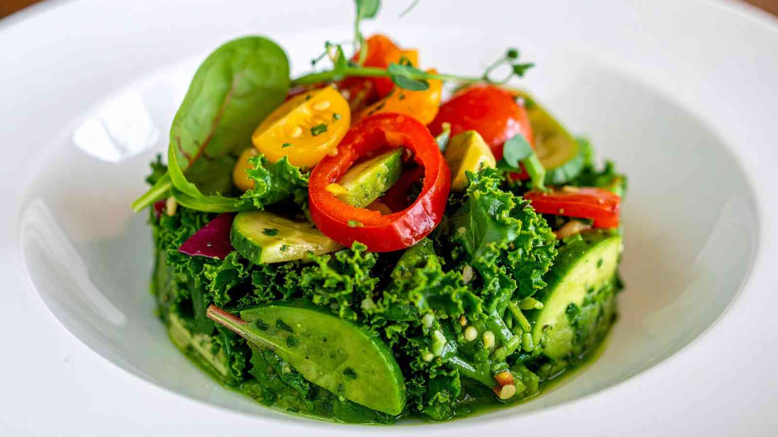 A plate of fresh salad with leafy greens, sliced avocado, cherry tomatoes, and red pepper rings, garnished with herbs.