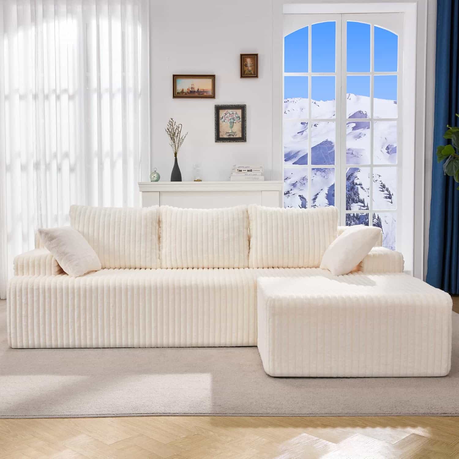 A cream-colored sectional sofa with striped upholstery sits in a bright living room with a window showing a snowy mountain view.