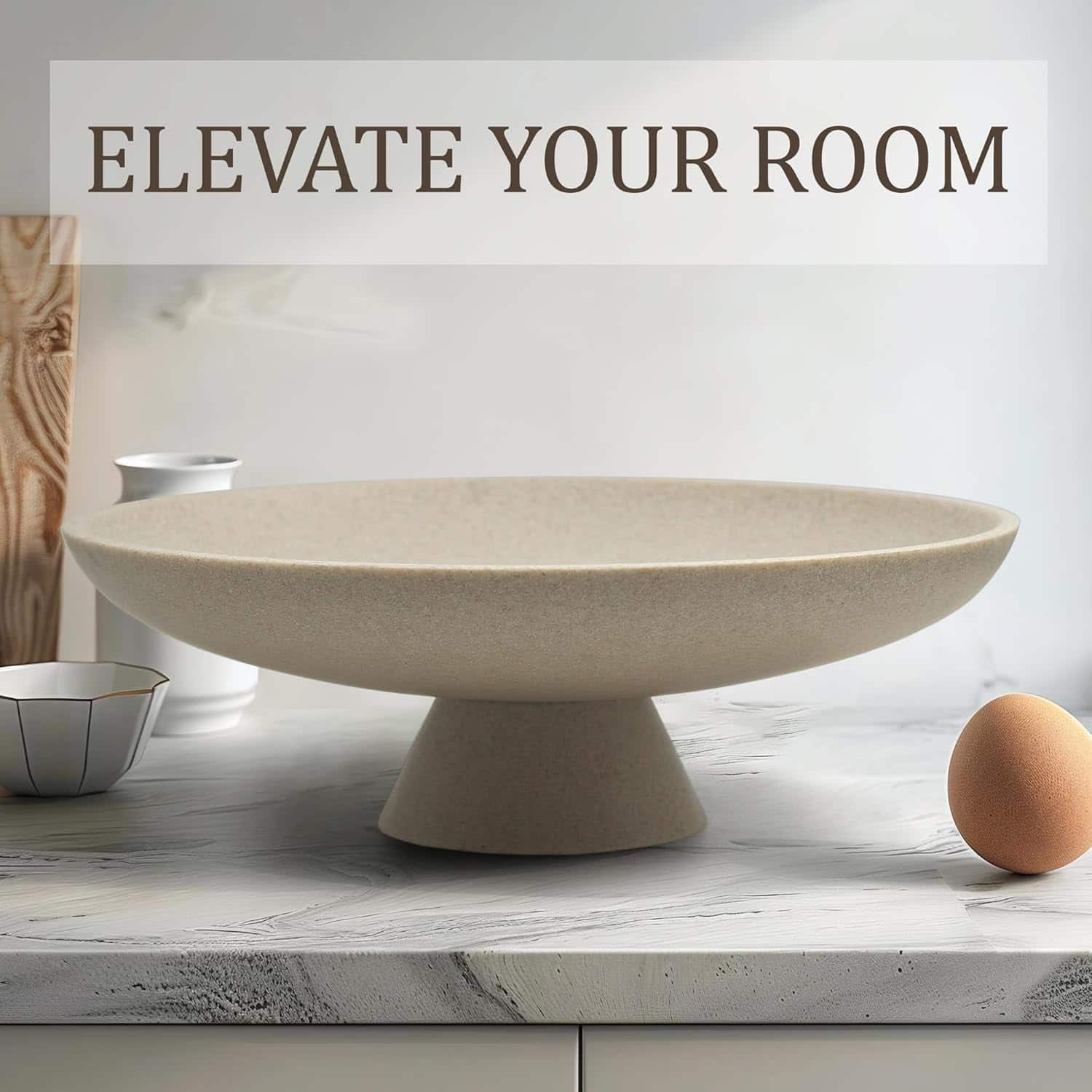 A beige pedestal bowl sits on a marble countertop next to a brown egg and a metal measuring cup, with "ELEVATE YOUR ROOM" text above.