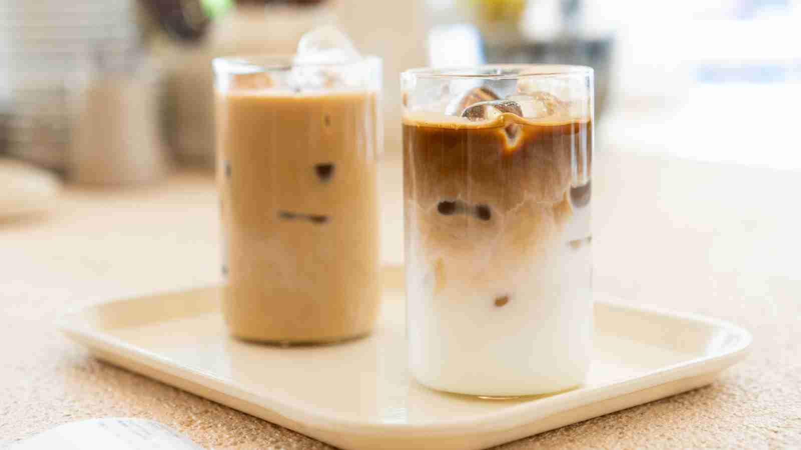 Two glasses of iced coffee drinks on a rectangular tray; one appears mixed, while the other shows a layered effect of milk and coffee.