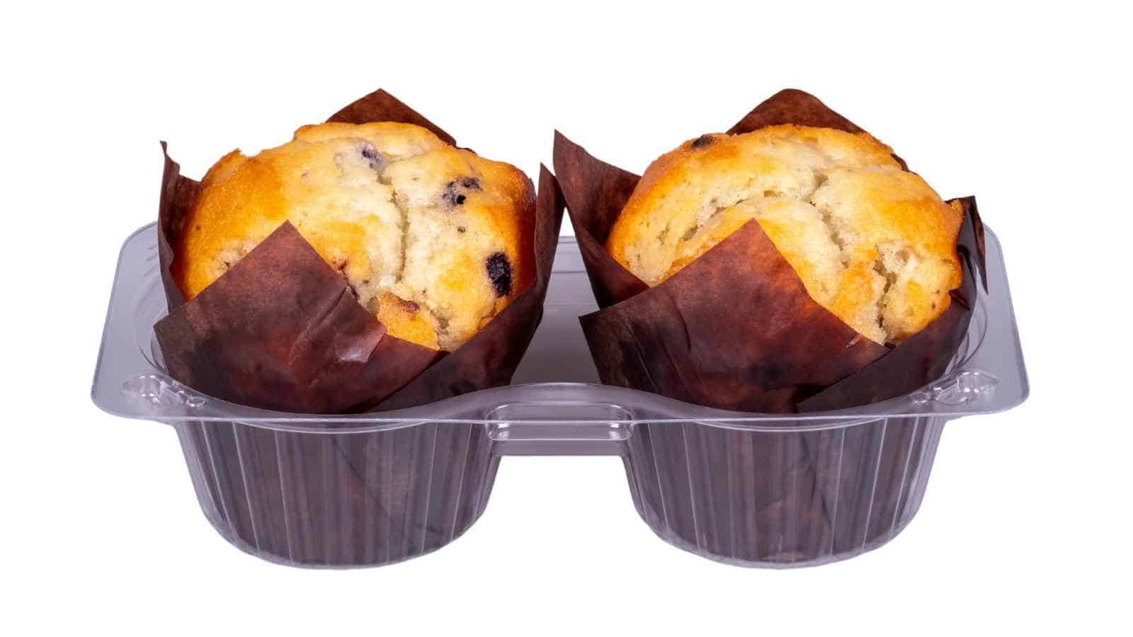 Two blueberry muffins in brown paper wrappers, placed in a clear plastic container, isolated on a white background.