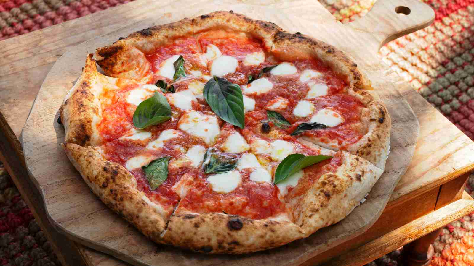 A Margherita pizza with tomato sauce, melted mozzarella cheese, and fresh basil leaves on a wooden pizza peel.