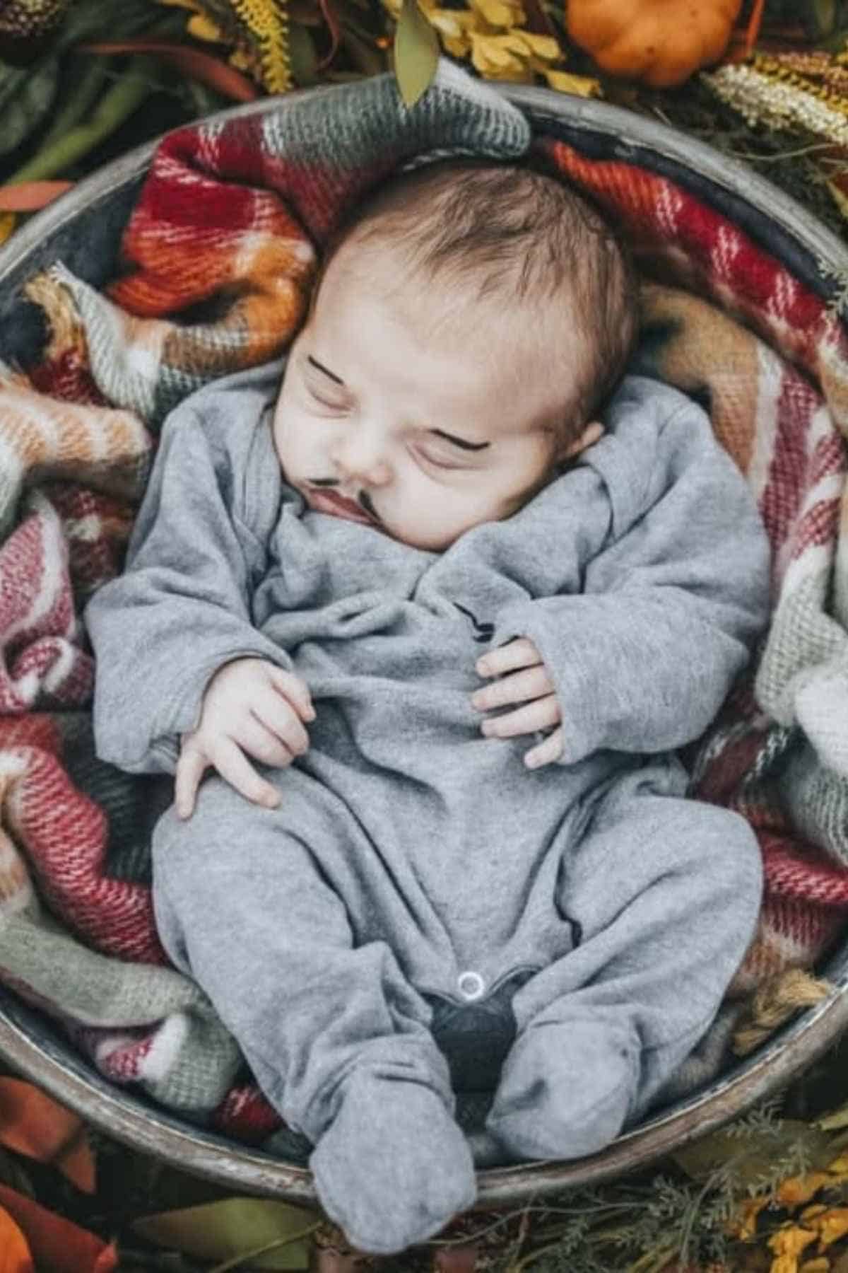 A baby dressed in a colorful piñata costume lies on a white fluffy rug, surrounded by assorted candy pieces.
