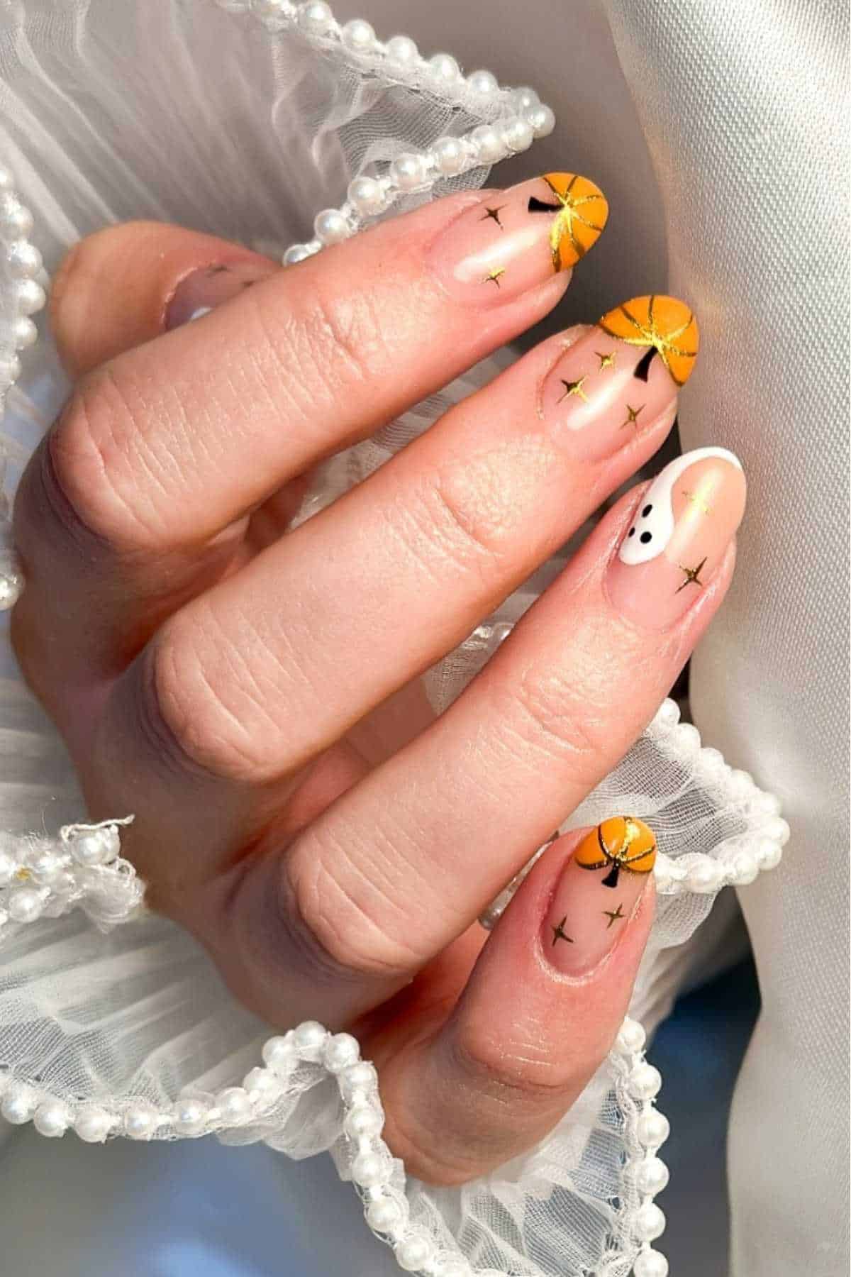 A hand with almond-shaped nails featuring orange slices, gold star accents, and one nail with a smiley face, against a white ruffled and pearl-decorated fabric background.