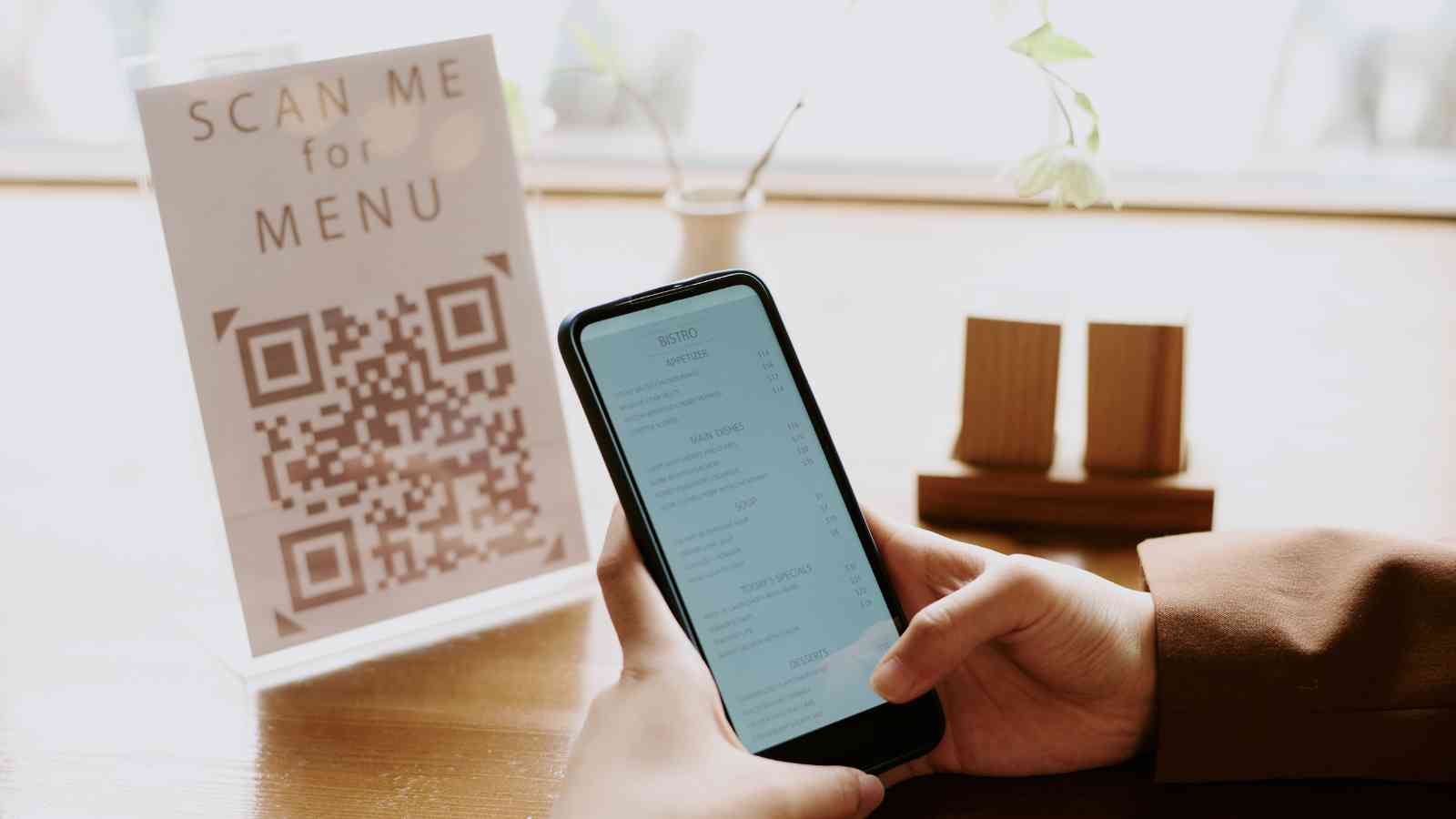 A person holding a smartphone views a digital menu after scanning a QR code sign on a restaurant table.