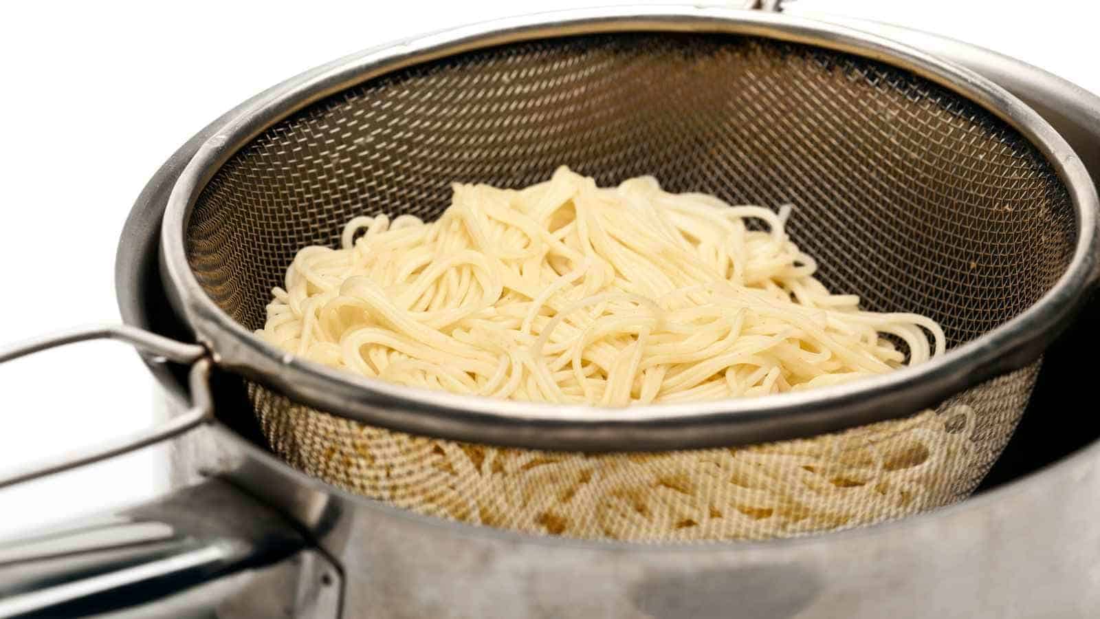 Cooked spaghetti noodles are draining in a metal mesh strainer placed over a pot.