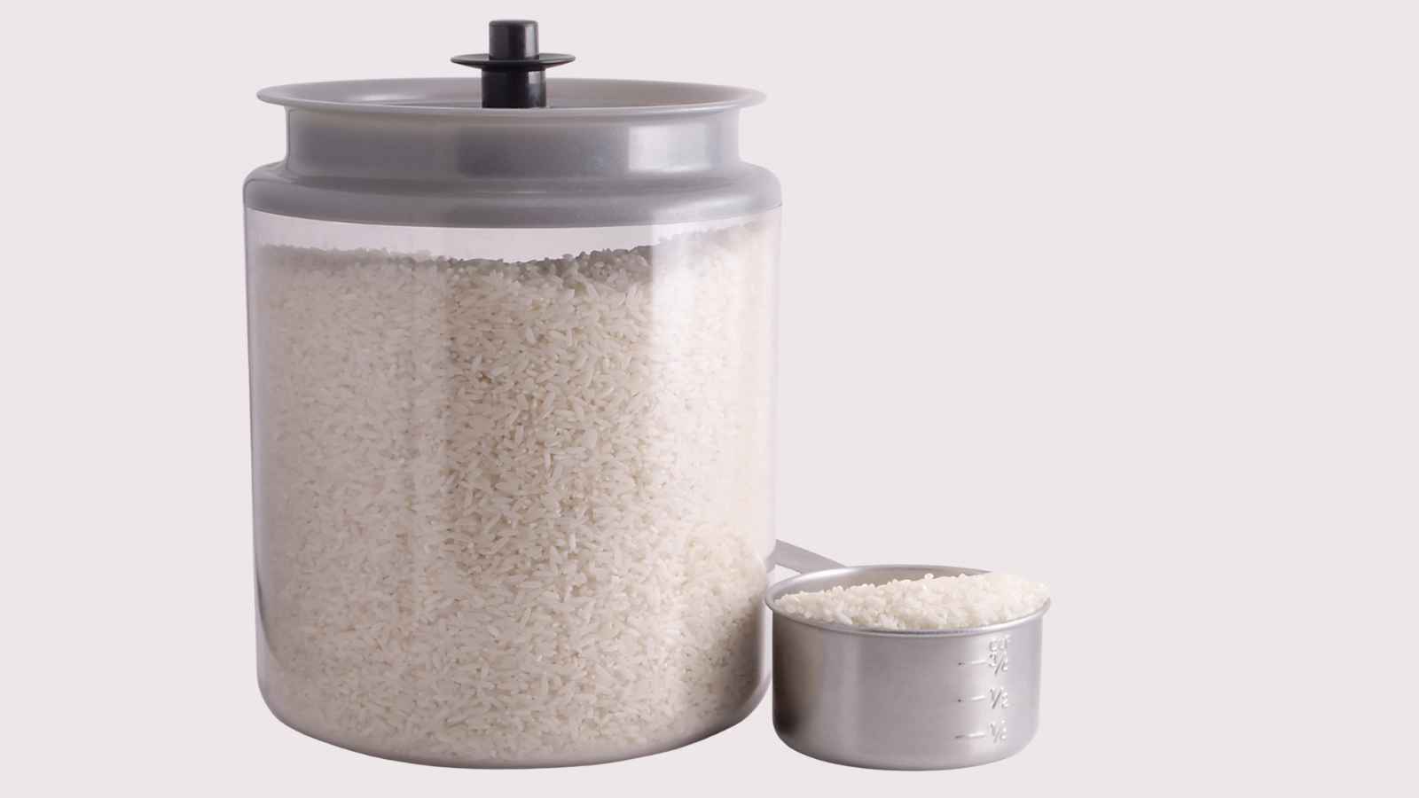 A transparent container filled with uncooked white rice next to a metal measuring cup holding a smaller portion of rice.