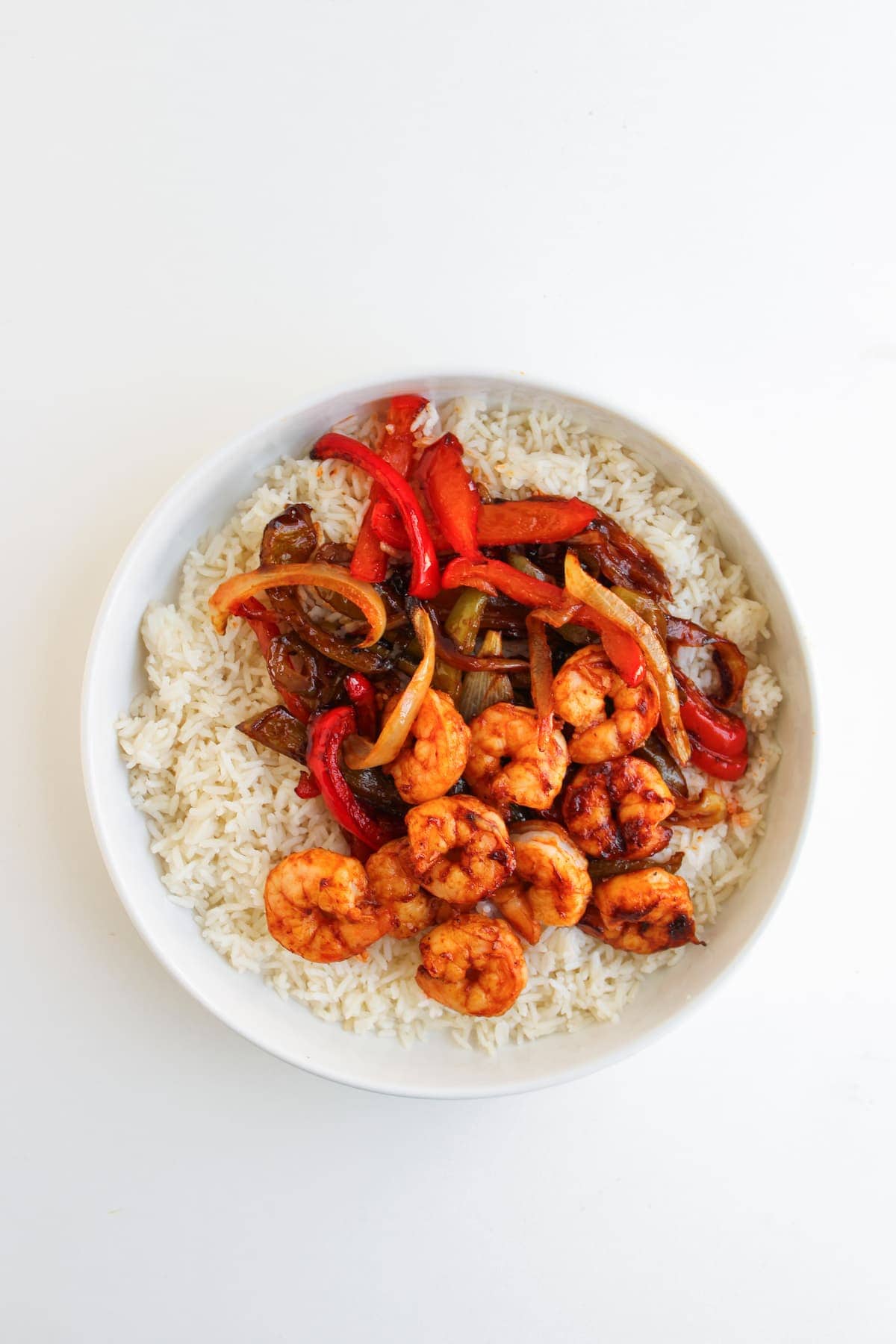 A white bowl filled with white rice, topped with cooked shrimp, red bell peppers, onions, and brown sauce.