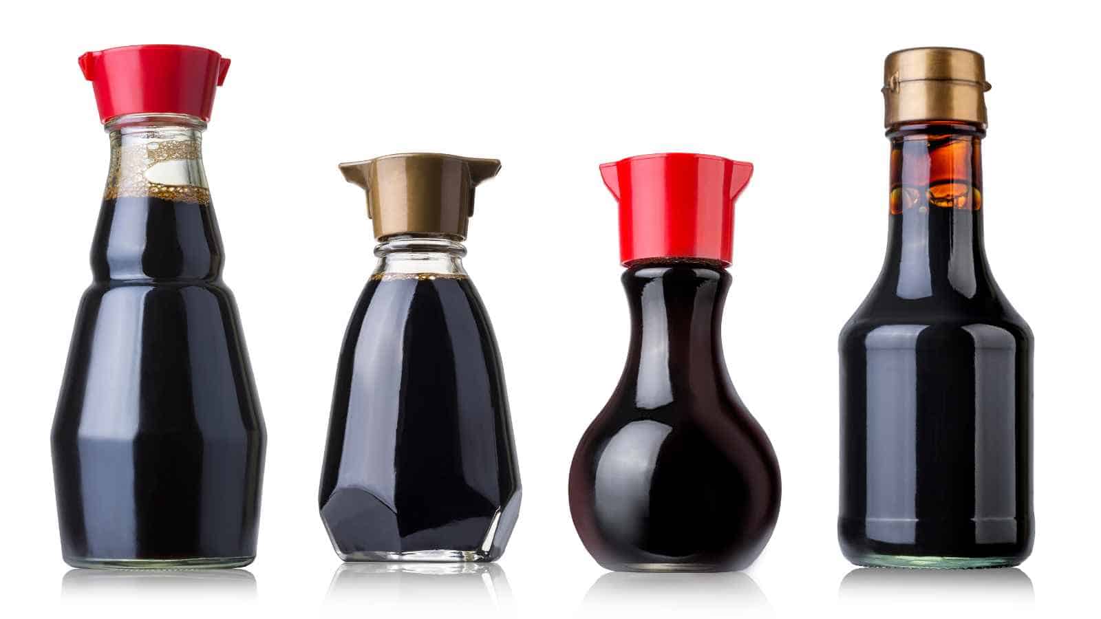 Four bottles of soy sauce in various shapes and sizes, each with a different colored cap, are arranged in a row on a white background.