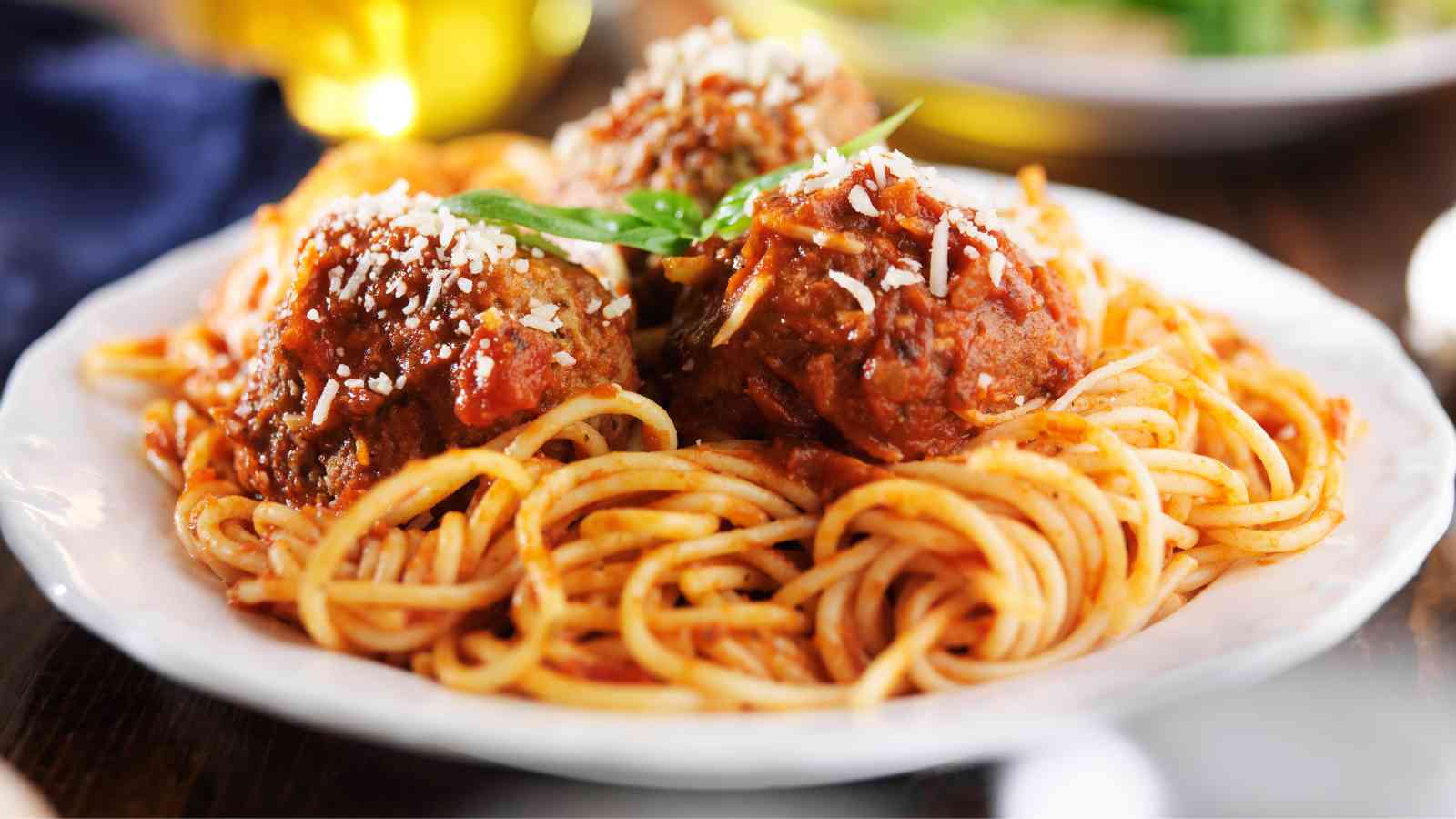 A plate of spaghetti topped with tomato sauce, meatballs, grated cheese, and a garnish of fresh herbs.