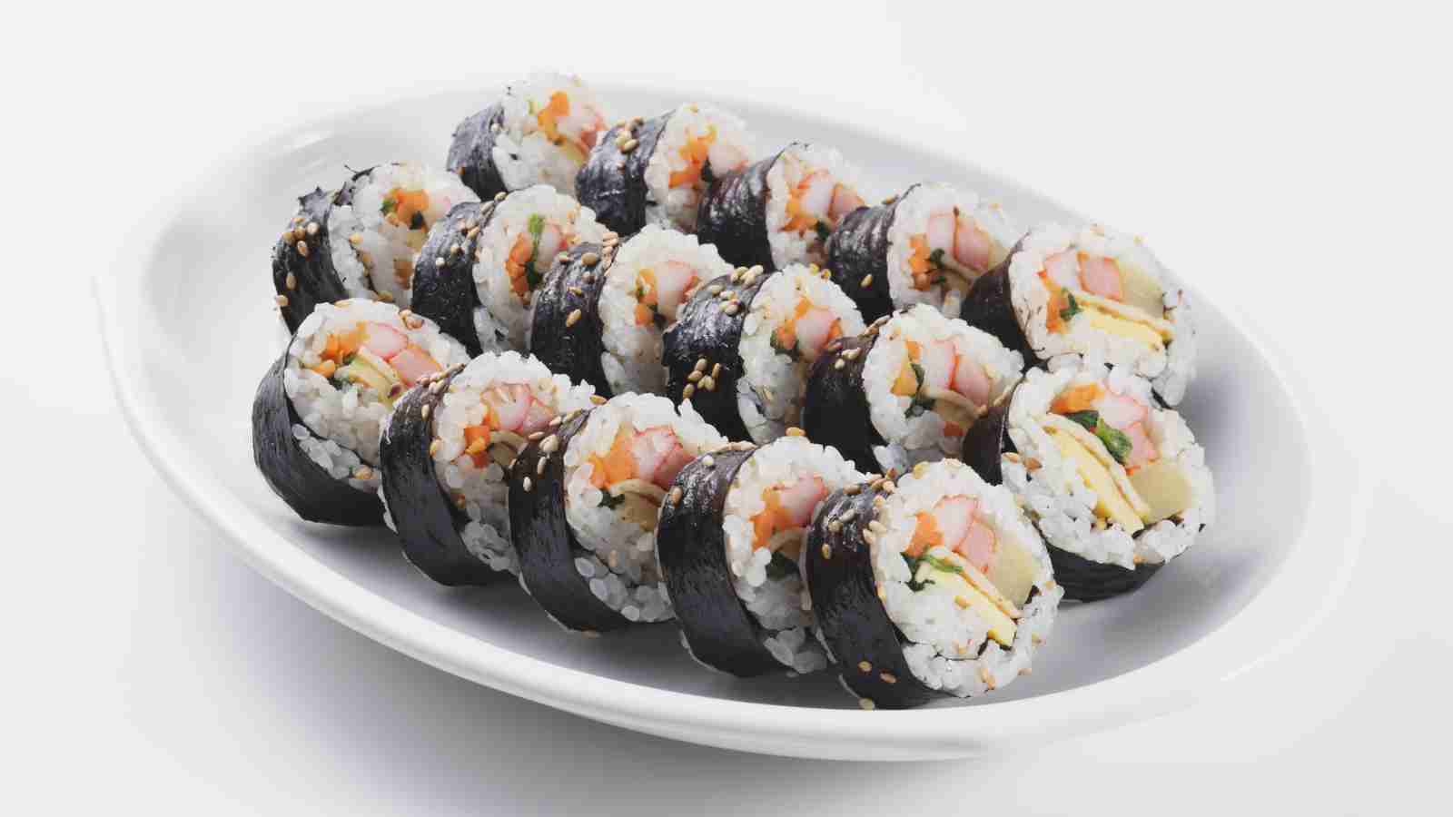 A white plate with neatly arranged slices of kimbap, a Korean dish made with rice, vegetables, and other fillings wrapped in seaweed.