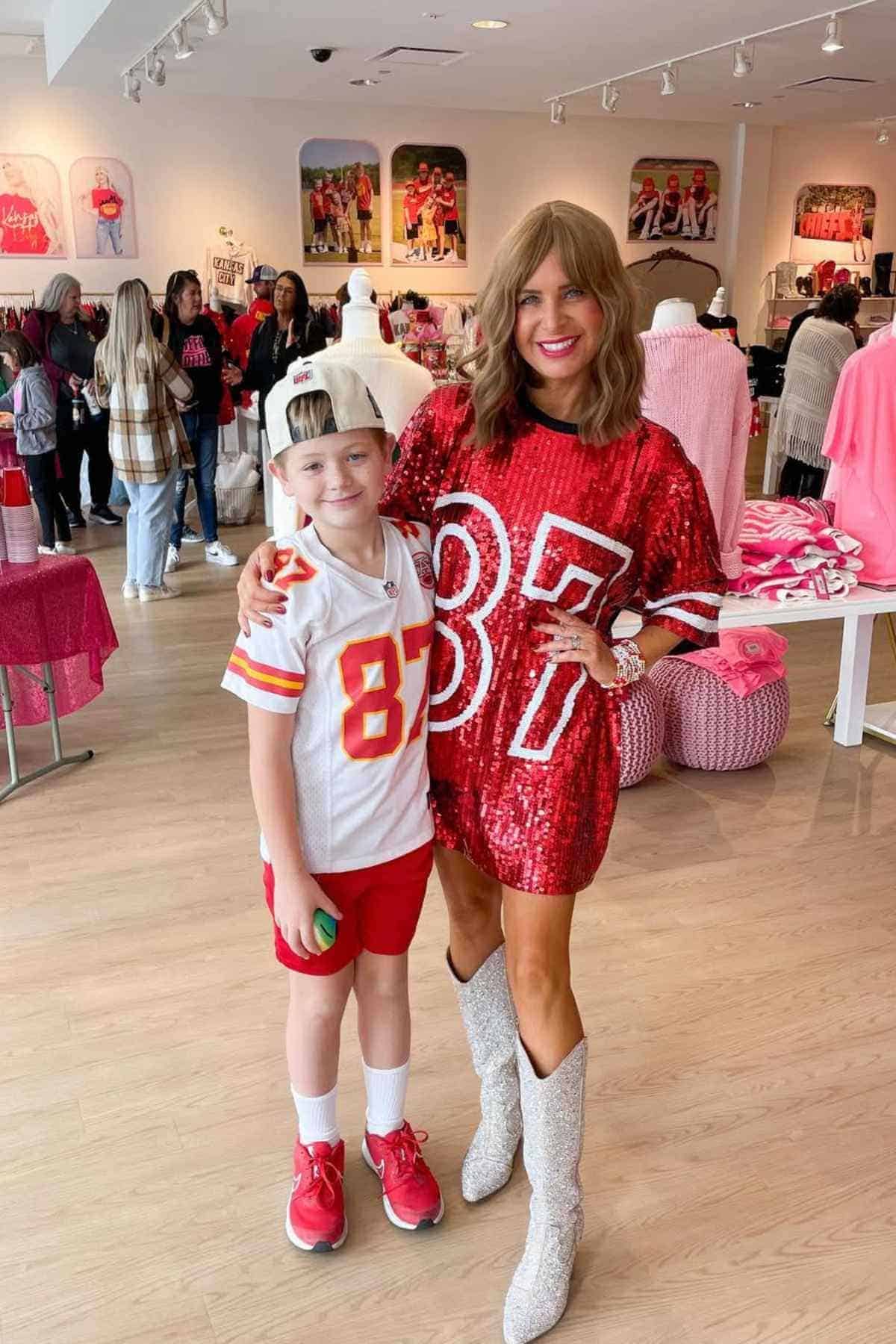 A woman in a red sequined "87" dress and a child in a white "87" jersey and red shorts pose together in a brightly lit clothing store.