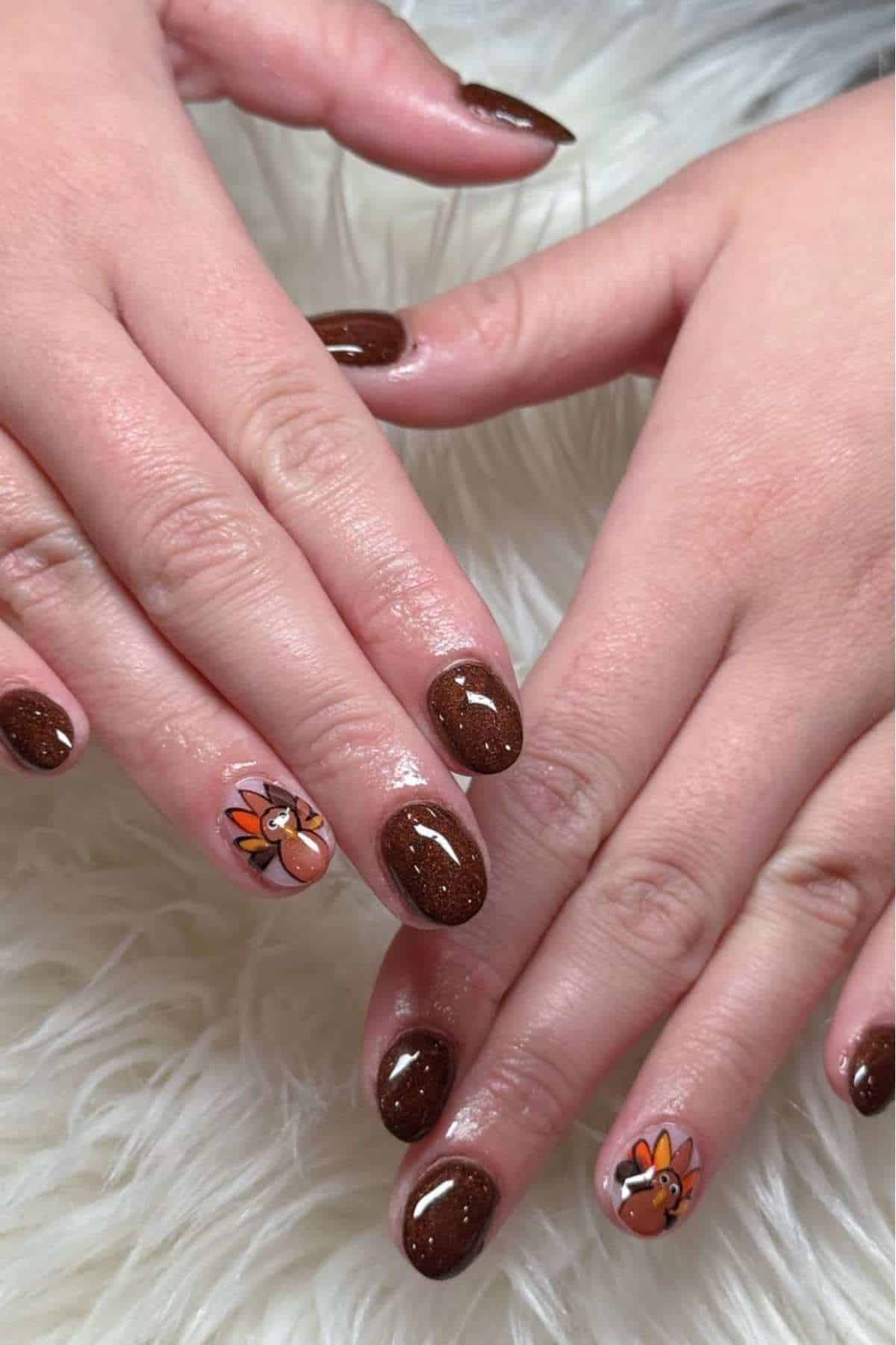 Hands with brown glittery nail polish; the ring fingernails have a painted cartoon turkey design. The hands are placed on a white, furry surface.