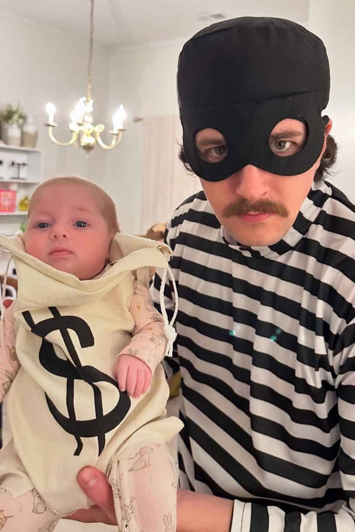 An adult dressed as a burglar holds a baby in a sack costume marked with a dollar sign.