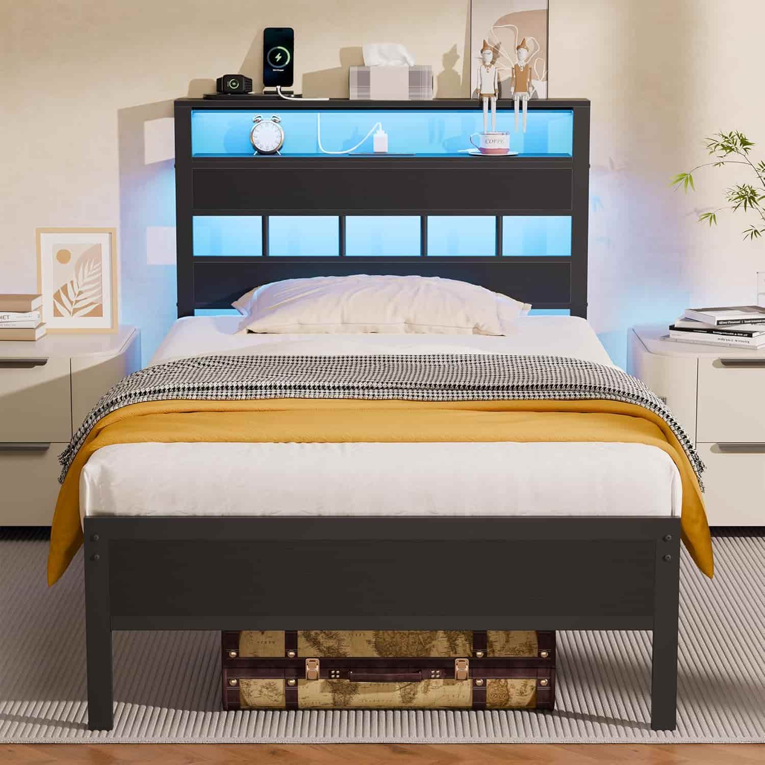 A modern bed with a dark headboard featuring blue LED lighting, two nightstands, and a decorative trunk underneath the bed.